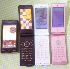 five different cell phones are lined up on a tableclothed surface, one is pink and the other is white