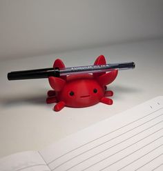 a red plastic crab with a pen on it's head and writing paper in front of it