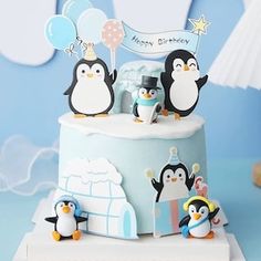 a birthday cake decorated with penguins and balloons