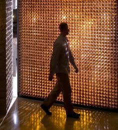 a man walking past a large wall made out of glass bottle caps in the dark