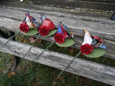 three red roses sitting on top of a wooden bench