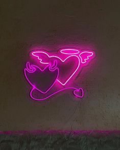 a neon sign with two hearts and an angel on it's side, against a wall