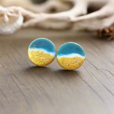 two yellow and blue earrings sitting on top of a wooden table next to a seashell