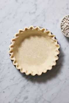 an uncooked pie crust next to a bowl with seeds in it on a marble surface