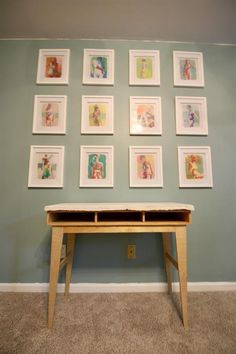 there are many framed pictures on the wall above a small wooden table with two drawers