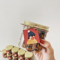 a person holding a jar with cookies in it next to some gold coins on the table