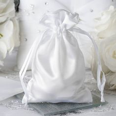 a white satin bag sitting on top of a table next to flowers and other items