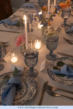 the table is set with blue and white dishes, silverware, candles, and napkins