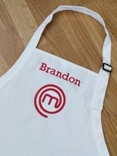 a white apron with the word brandon on it sitting on a wooden floor next to a pair of scissors