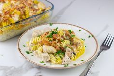 a plate of pasta with chicken and parsley on it next to a casserole dish