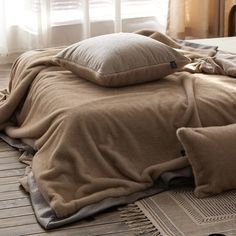 an unmade bed with pillows and blankets on the floor in front of a window