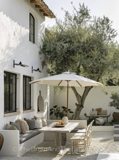 an outdoor dining area with table, chairs and umbrella in front of a white house