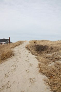 a path leading to a house on the beach with footprints in the sand and grass