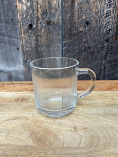 a clear glass mug sitting on top of a wooden table next to a wood wall