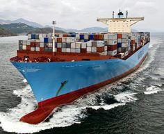 a large blue and red container ship in the middle of the ocean with mountains in the background