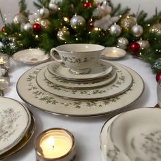 a white table topped with plates and cups next to a christmas tree filled with ornaments