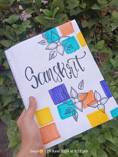 a hand holding up a notebook with the words sunset written on it in front of green leaves