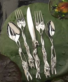 four forks and two spoons sitting on top of a leafy green surface with fish in the background