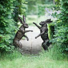 two statues of rabbits are in the middle of some bushes and trees, one is jumping