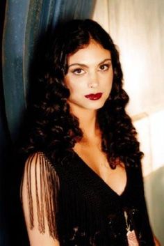 a woman with long curly hair wearing a black dress and red lipstick is posing for the camera