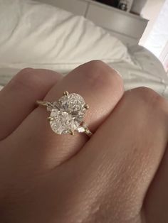 a woman's hand with a diamond ring on top of her finger, in front of a bed