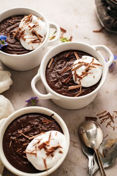 three white bowls filled with chocolate pudding on top of a table next to spoons