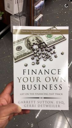 a person holding up a book with money on the front and back cover that reads finance your own business get on the financial fast track