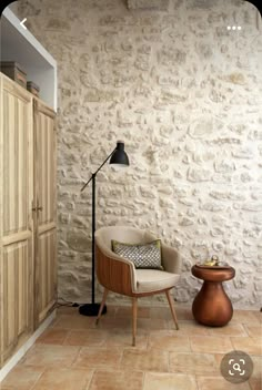 a living room with a chair, lamp and cupboards in front of a stone wall