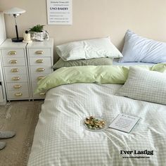 a bed with green and white comforter next to a lamp on a dresser in a bedroom