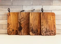 three wooden cutting boards sitting on top of a counter next to a brick wall with deer and pine trees painted on them