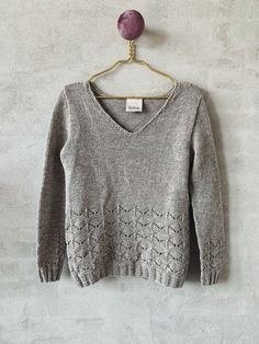 a gray sweater hanging on a wall with a purple ball attached to the top of it