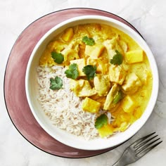 a white bowl filled with rice and curry next to a fork on top of a table