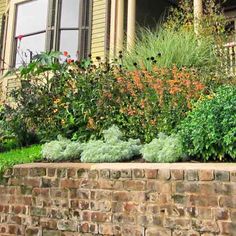 a brick planter filled with lots of flowers next to a house and window sill