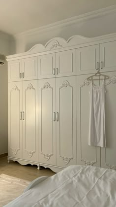 a white bed sitting next to a large white cabinet in a room with hard wood floors