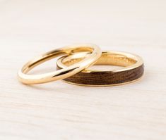 two gold wedding rings sitting side by side on top of a wooden table with white background