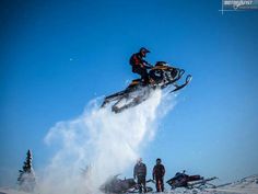 a person jumping in the air on a snowmobile with other people watching from behind