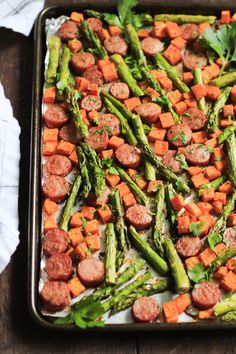 asparagus, sausage and carrots in a baking pan on a wooden table