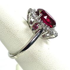 1970s Sterling and synthetic ruby cocktail ring. Oval faceted synthetic ruby in a shallow basket setting surrounded by a halo of clear CZs, atop a simple smooth shank. The stone is absolutely spectacular, a rich, saturated, delicious ruby red with glints of pink and purple deep within. The brilliant clear CZs surrounding it frame and accentuate its deep resonant hue. A perfect cocktail ring for any occasion, fancy or otherwise! Signed "Sterling". Face of ring, 0.65"L x 0.6"W. Size 6.5 Dazzling Oval Ruby Ring, Formal Halo Jewelry With Lab-created Ruby, Elegant Formal Ruby Halo Ring, Dazzling Oval Ruby Ring With Prong Setting, Formal Lab-created Ruby Ring With Prong Setting, Formal Oval Ruby Ring With Center Stone, Formal Ruby Ring With Diamond Halo, Classic Oval Lab-created Ruby Diamond Ring, Formal Ruby Cluster Ring With Center Stone