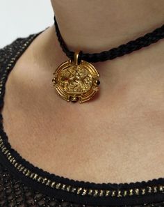 "Inspired by ancient Roman jewelry, this golden pendant sits on a braided cord, emblazoned with a mythological vignette, featuring a winged angel and an oxen. From the emblem to the shield-like shape of the pendant, it has an Etruscan feel. It sits on a vegan leather braided cord, which has a magnetic closure in the back. Pendant measures about 31 mm wide x 28 mm high, and the cord is 13.5\" long. ** The Vintage Dolce & Gabbana Metallic Knit Top pictured is also available: verybreezy.com/product Fae Jewelry, Leather Braiding, Ancient Style Gold Pendant Jewelry, Ornate Brass Necklace With Intricate Design, Modest Jewelry, Ancient Bronze Medallion Necklace, Ornate Bronze Brass Necklace, Ceremonial Historical Pendant Jewelry, Roman Necklace