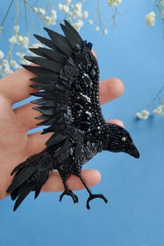 a hand holding a small black bird on it's finger with flowers in the background