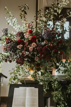 an open book sitting on top of a table next to flowers and greenery in front of a window