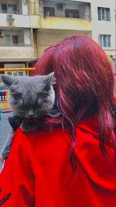 a woman with red hair is holding a gray cat in her arms and looking at the camera