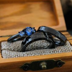 two black rings with blue stones are sitting in a wooden box