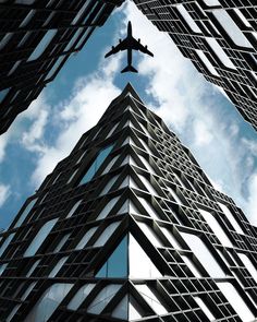 an airplane is flying in the sky over a building's glass facade and window panes