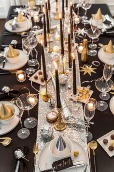 a long table is set with silver and gold place settings, black napkins, white plates, and candles