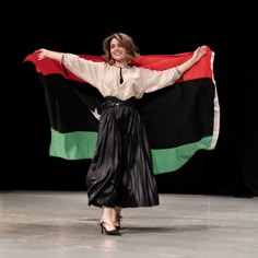 a woman holding a large flag on top of a black stage with other people in the background