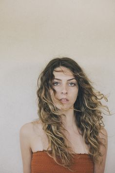 a woman with long hair standing in front of a white wall and looking at the camera