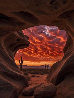 the sun is setting in between two large rocks, with a cactus and cacti