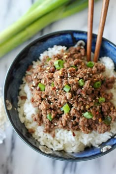 a blue bowl filled with rice and ground beef on top of a white table next to asparagus