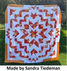 an orange and white quilt hanging from a line in the grass with text overlay that reads made by sandra tideman